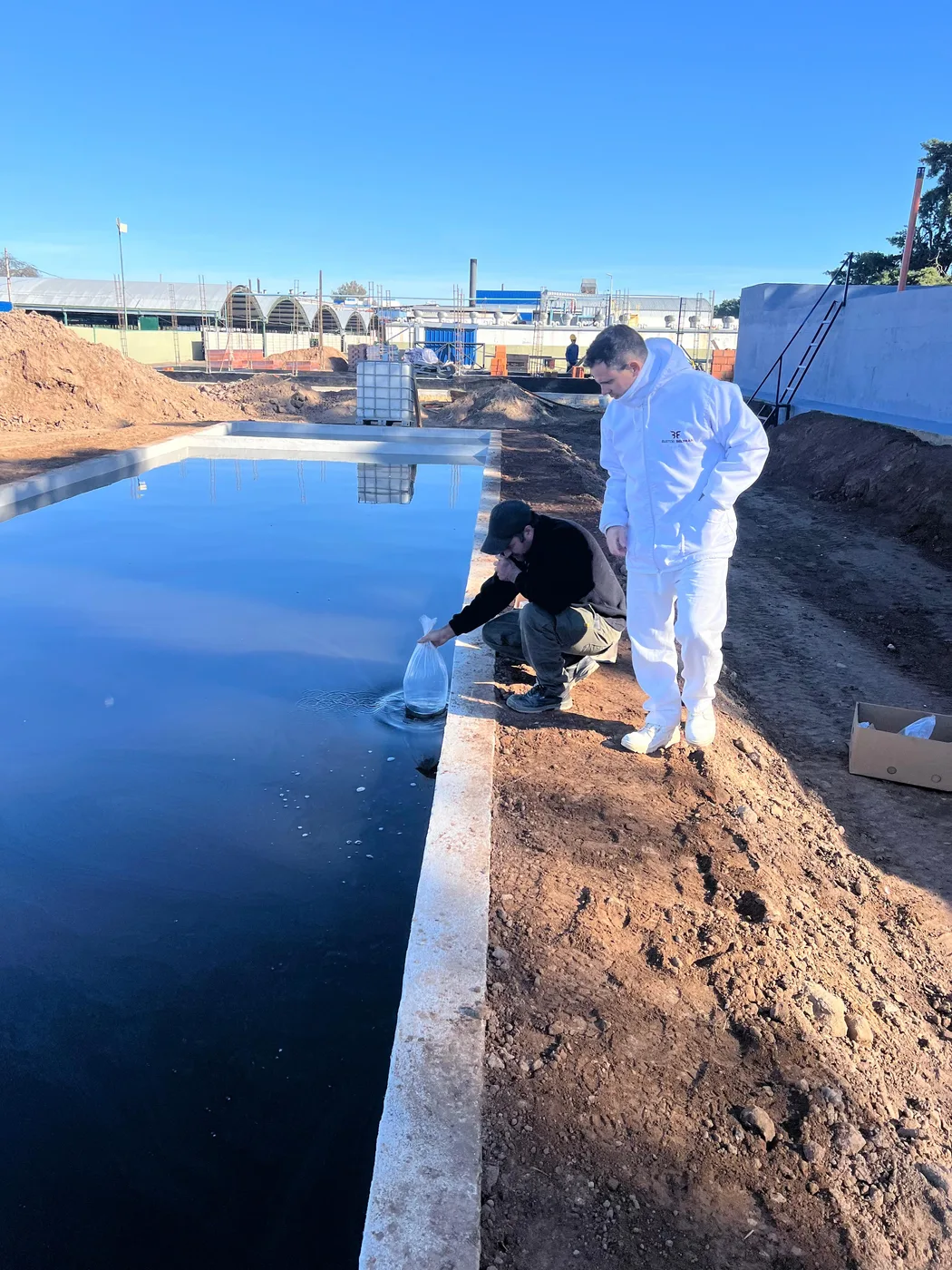 Dos operarios sembrando el preparado biológico en la laguna recién construida de una planta