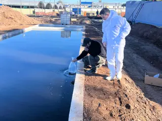 Dos operarios sembrando el preparado biológico en la laguna recién construida de una planta